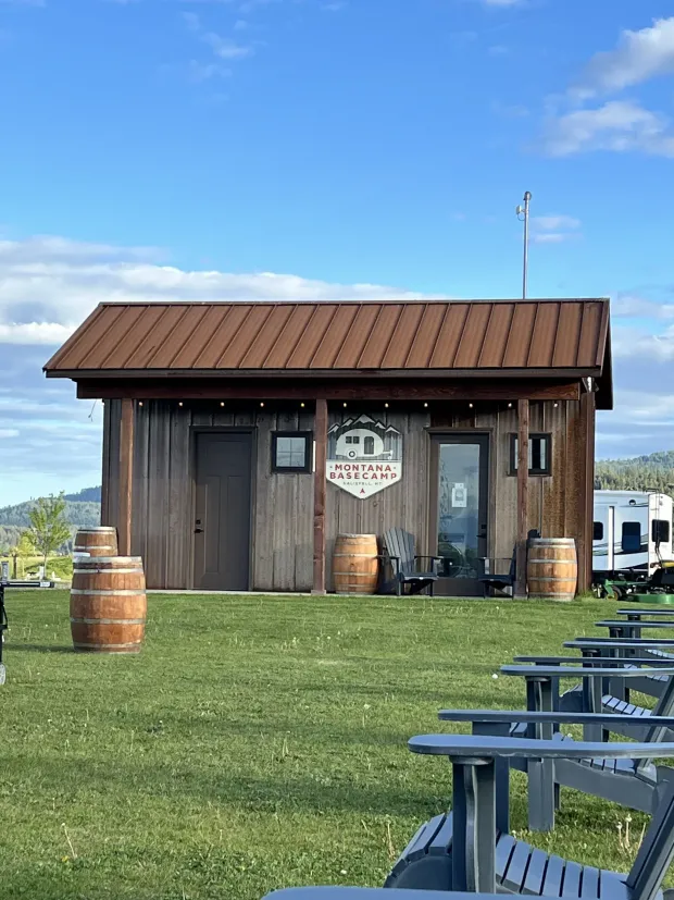 Rustic wooden tasting shed with barrels on a grassy lawn and picnic tables in front