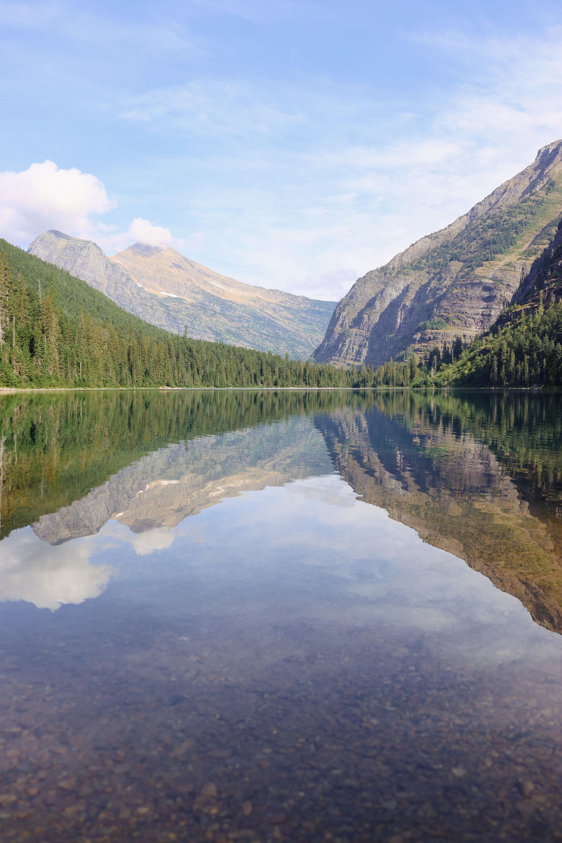 Mountain lake reflecting green forest and rocky peaks under a partly cloudy sky