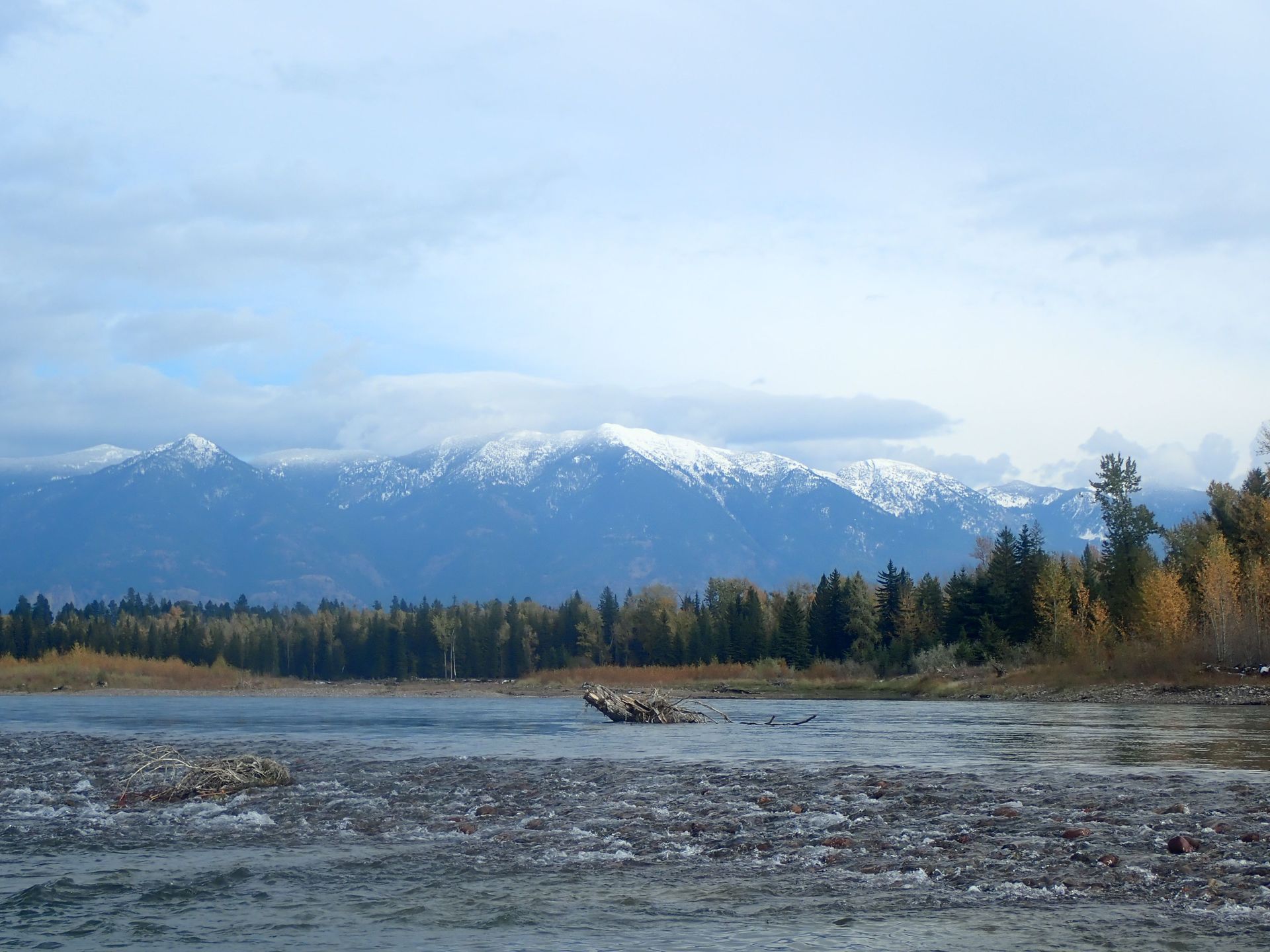 Snowy mountains beyond a forest and frozen river under a cloudy sky