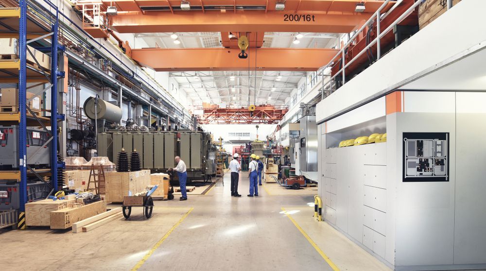 Large industrial factory with workers and machinery; orange crane.