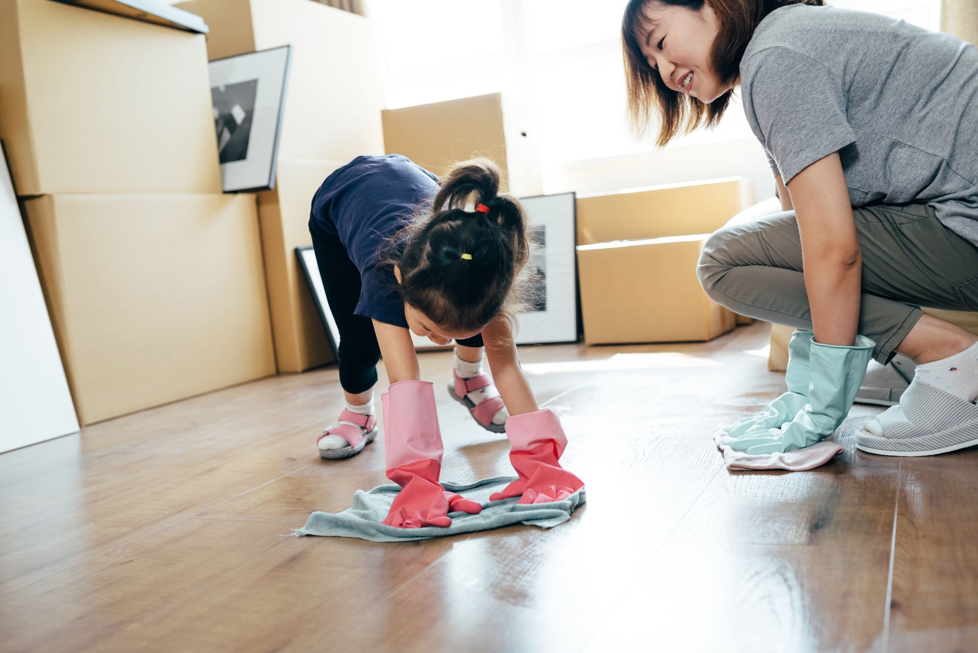 Outdoor floor cleaning with high pressure water jet. Child wearing gloves cleaning wooden floor with cloth while adult assists during home cleaning.