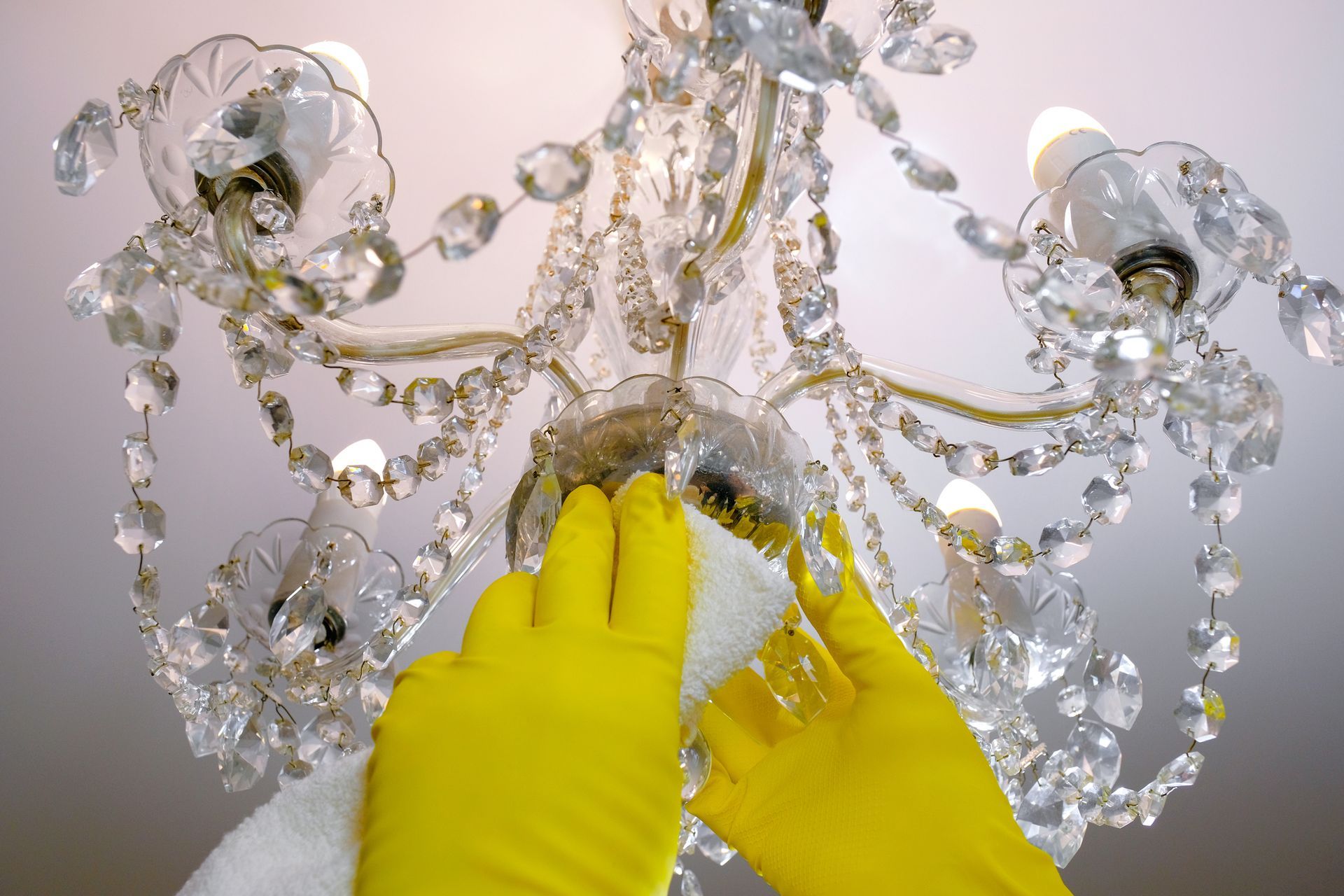 A person wearing yellow gloves is cleaning a chandelier.