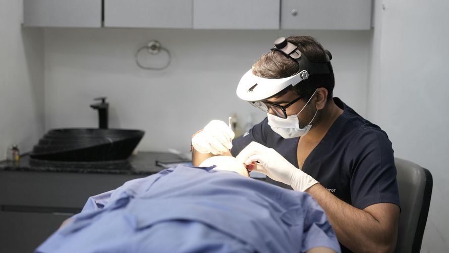 Dentist wearing a face shield and mask examines a patient in a dental clinic.