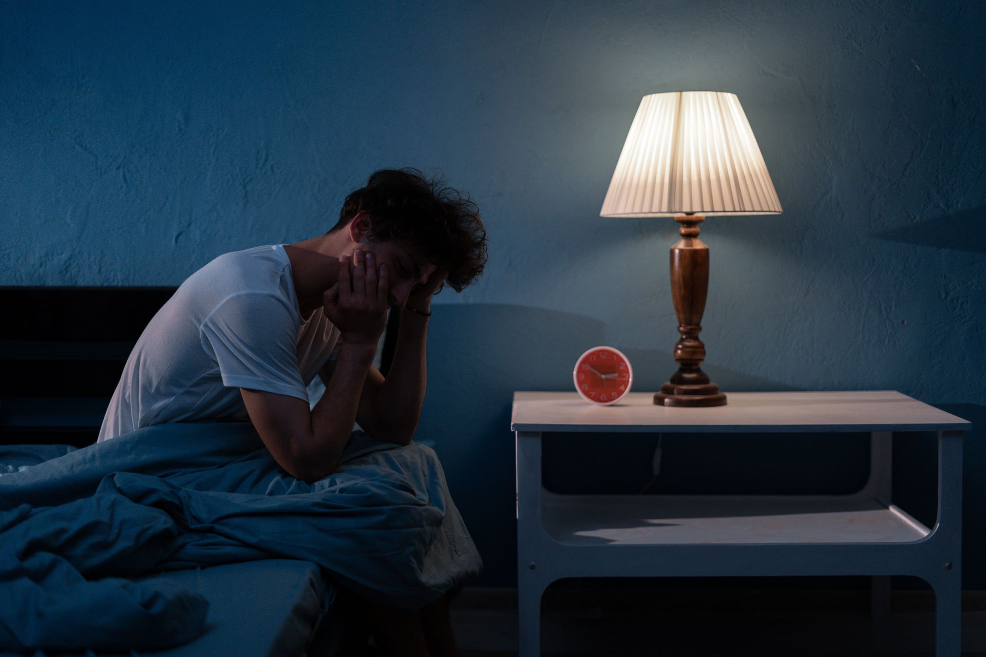 A man is sitting on a bed with his head in his hands.
