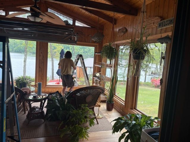 Covered porch with wicker chairs and hanging plants, overlooking a lawn and lake beyond.