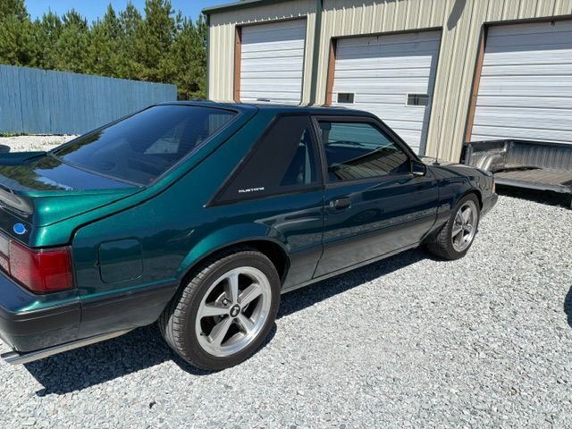 Teal two-door sports coupe parked beside garage bays on a gravel lot