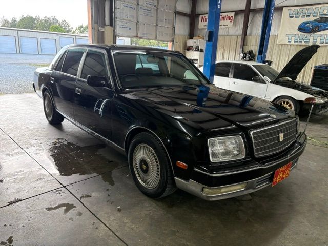 Black vintage sedan parked indoors in a garage, front-left view with chrome trim and wet floor.