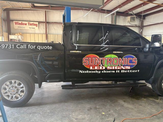 Black service truck with SunTroniques window tinting logo parked inside a garage