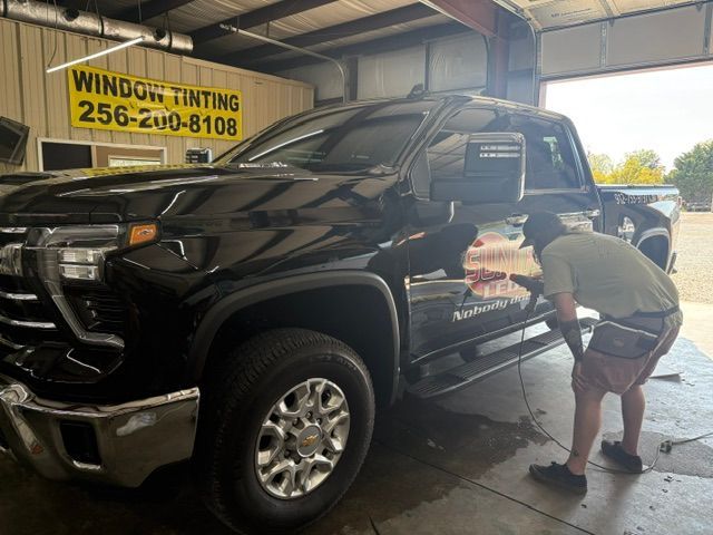 Black pickup truck being hand-washed in a garage with a window tinting sign.