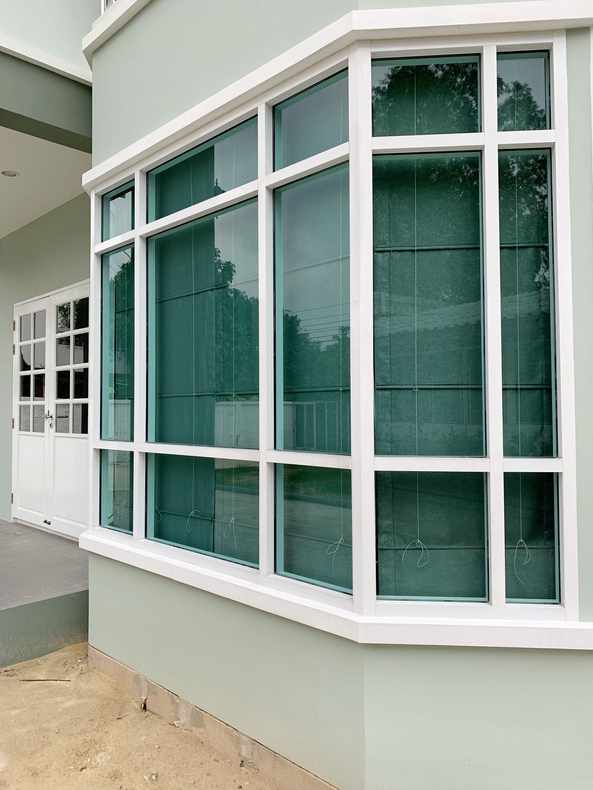 White-framed bay windows with green-tinted glass on a beige building exterior