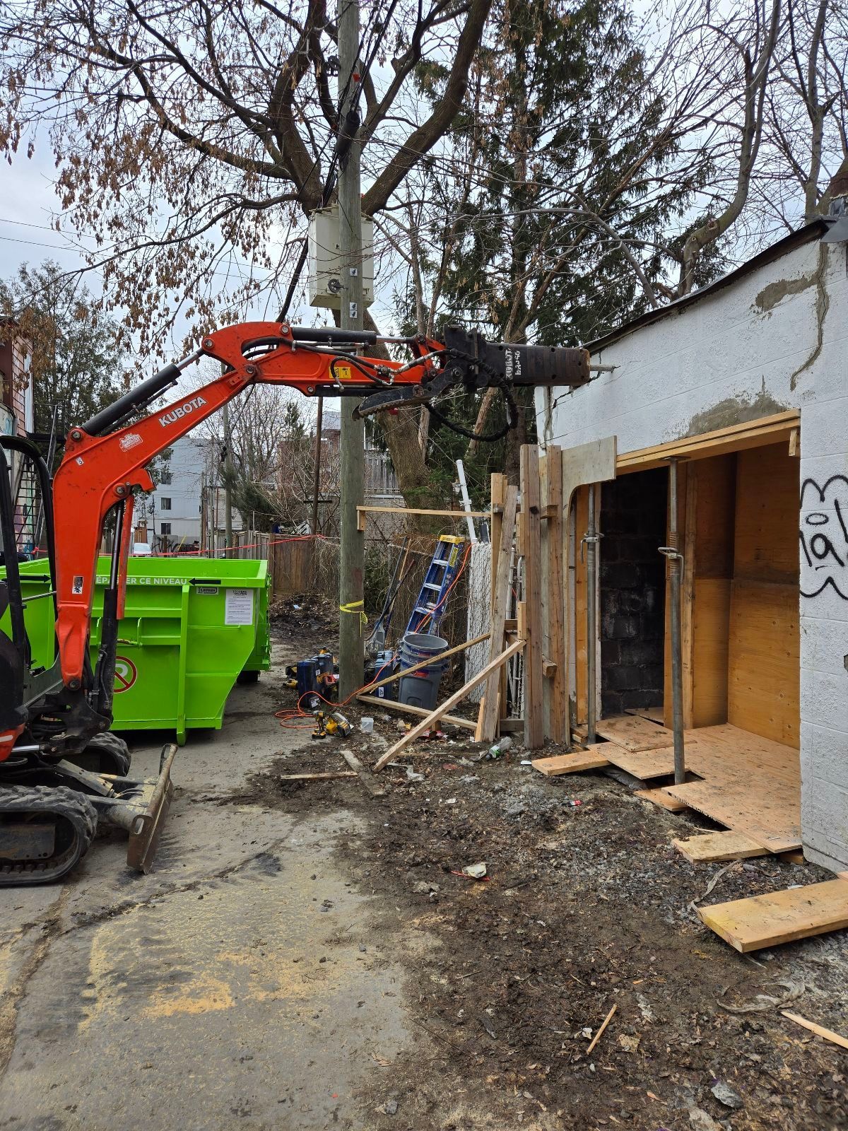 Une petite excavatrice orange est assise devant un bâtiment en construction.