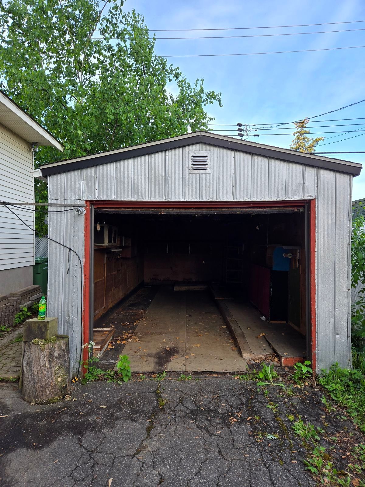 Un garage vide avec une porte rouge et une maison blanche en arrière-plan.