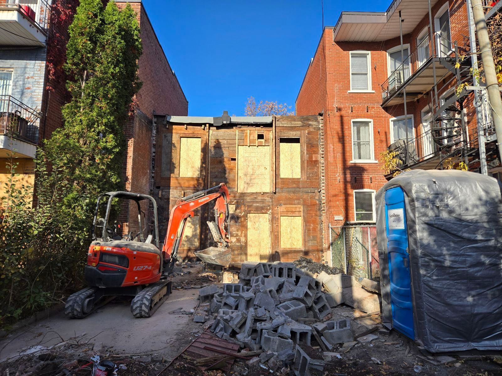 Une petite excavatrice est utilisée pour démolir un bâtiment en briques.