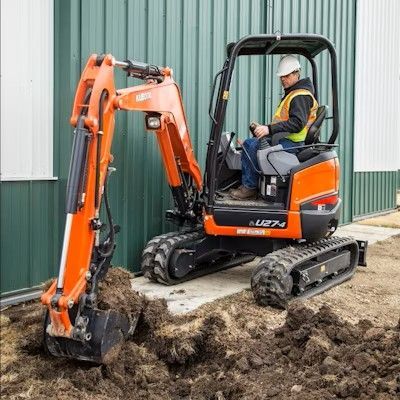 Un homme conduit une petite excavatrice orange dans un champ de terre.