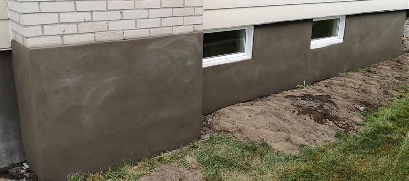 Mur de sous-sol avec revêtement imperméable gris sous parement de briques blanches et deux petites fenêtres