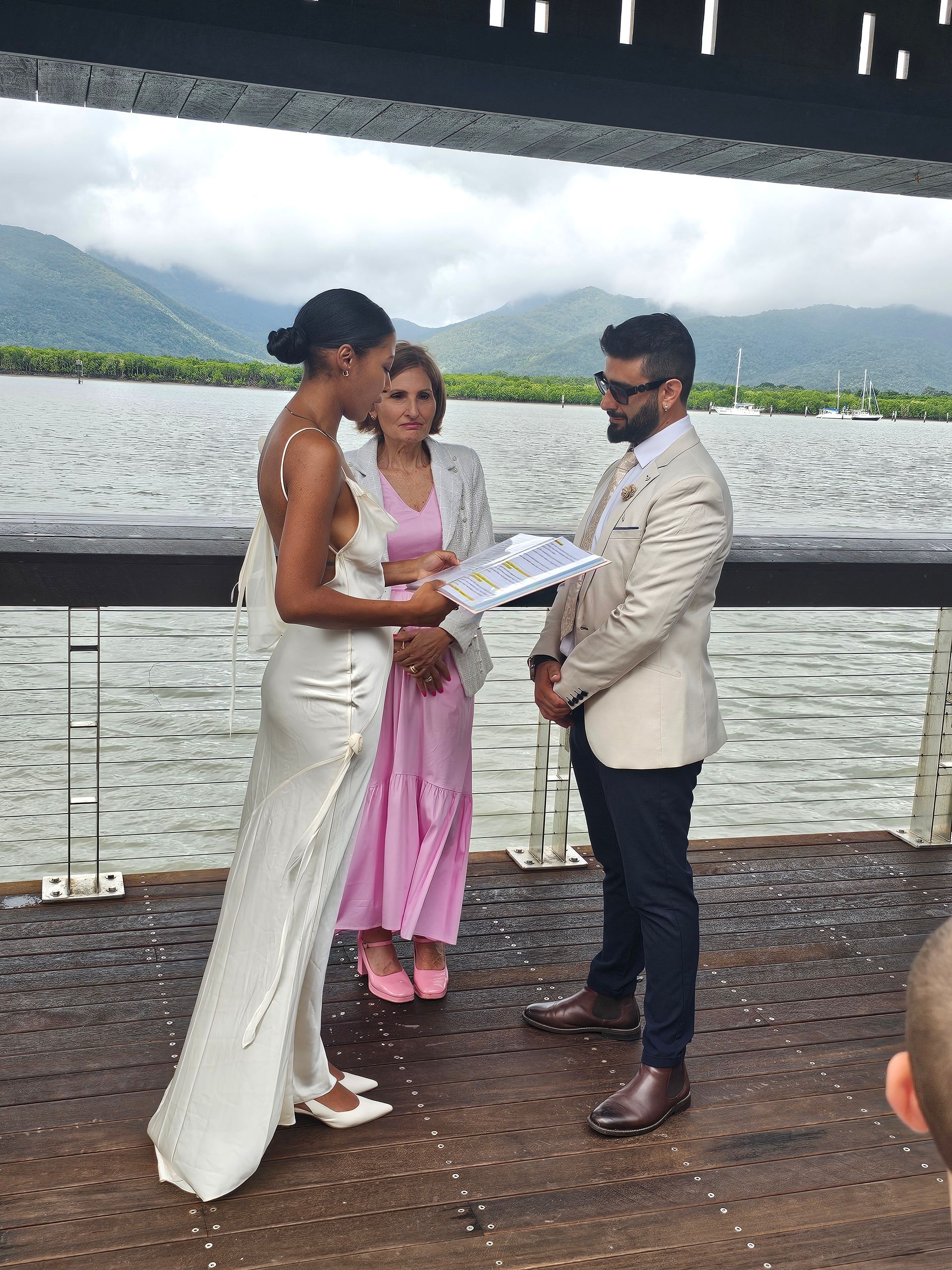 Wedding ceremony by a lakeside, with a couple and officiant exchanging vows under a canopy.