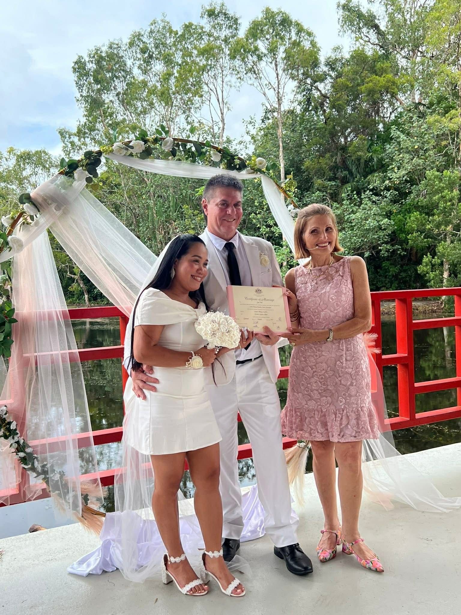 Three people posing at a wedding arch with red railings outdoors — GinaS Cairns Tropical Weddings in Parramatta Park, QLD