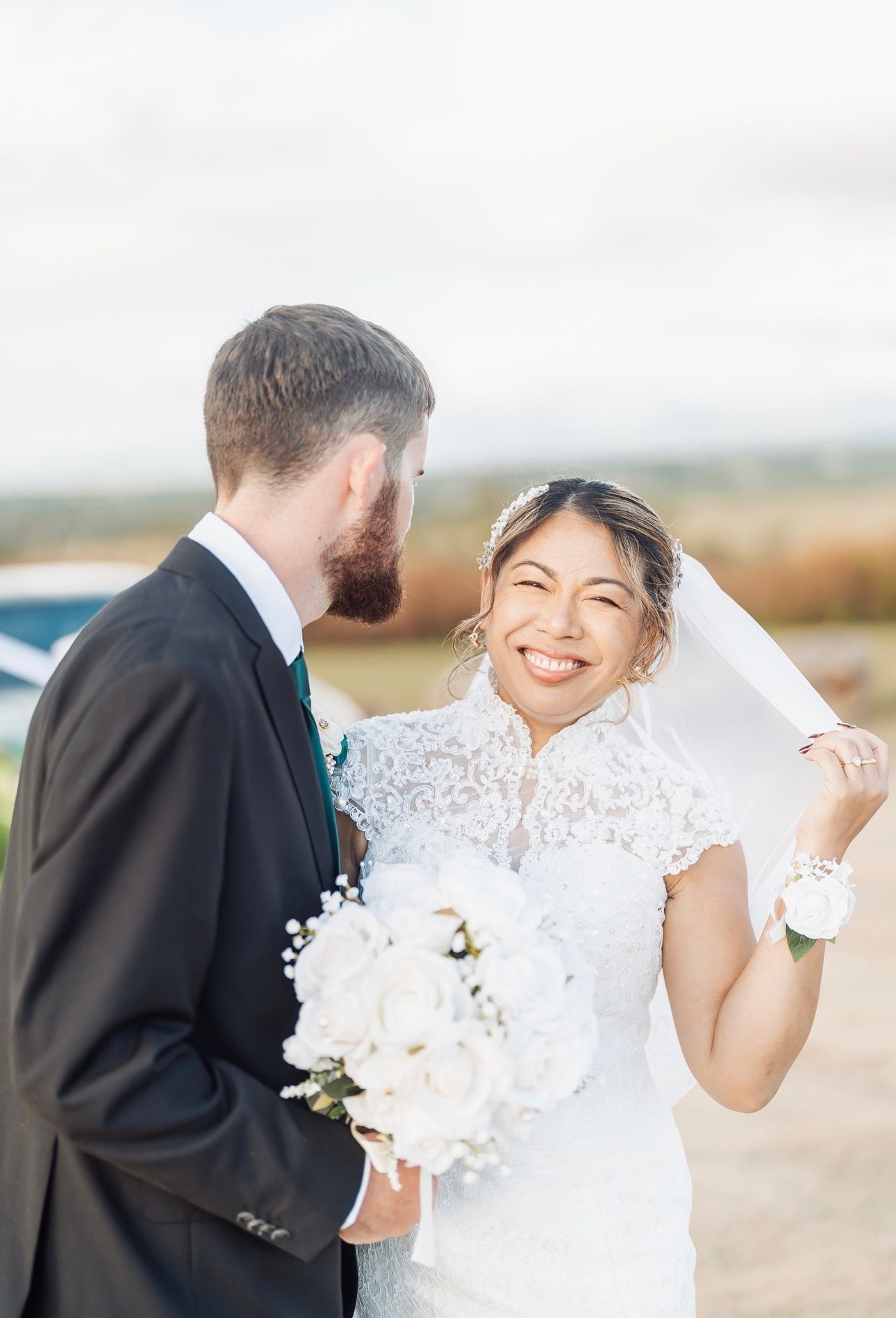 Bride smiling and holding bouquet beside groom in a black suit outdoors near water — GinaS Cairns Tropical Weddings in Parramatta Park, QLD