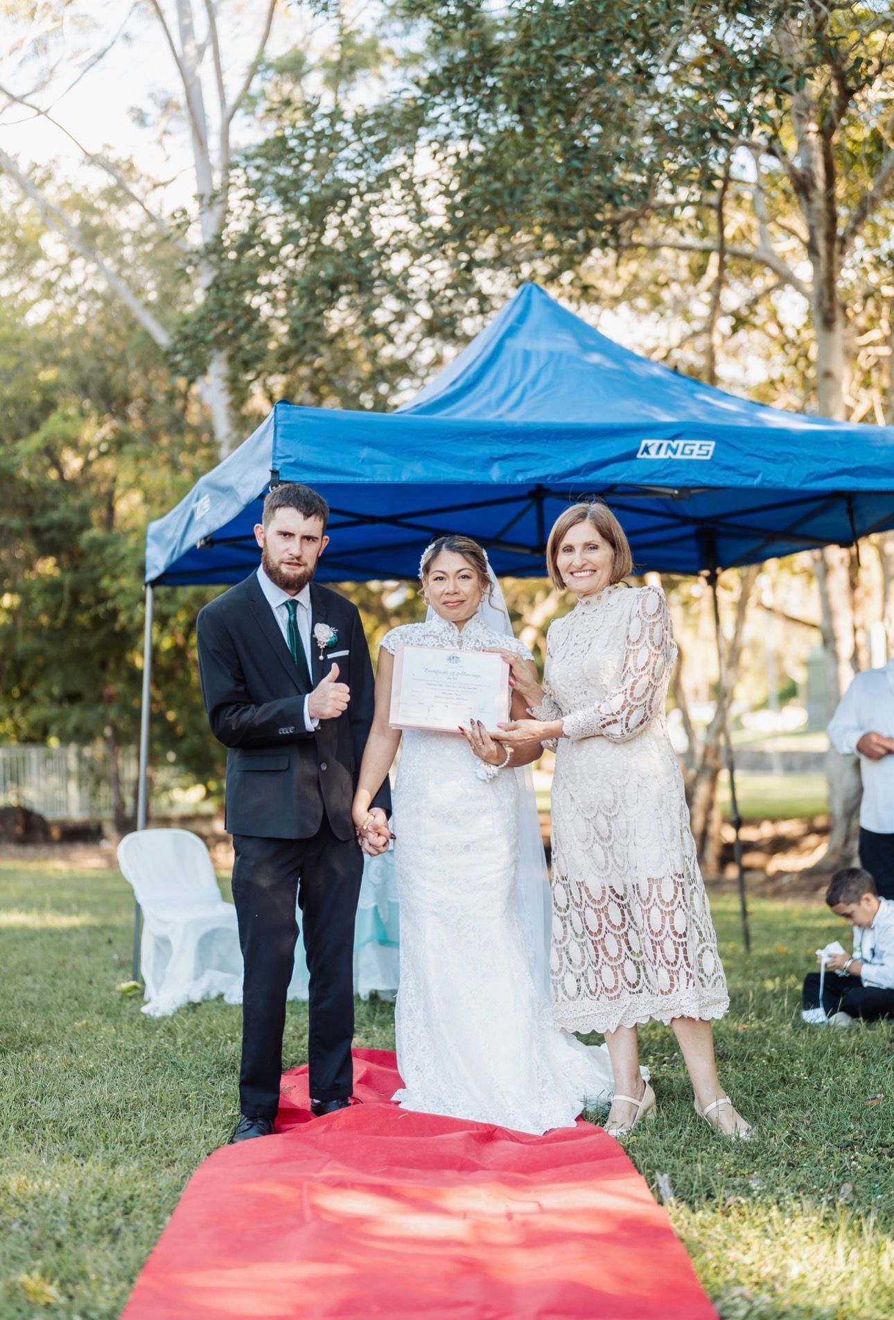 Wedding couple posing with officiant under a blue canopy on a red carpet outdoors