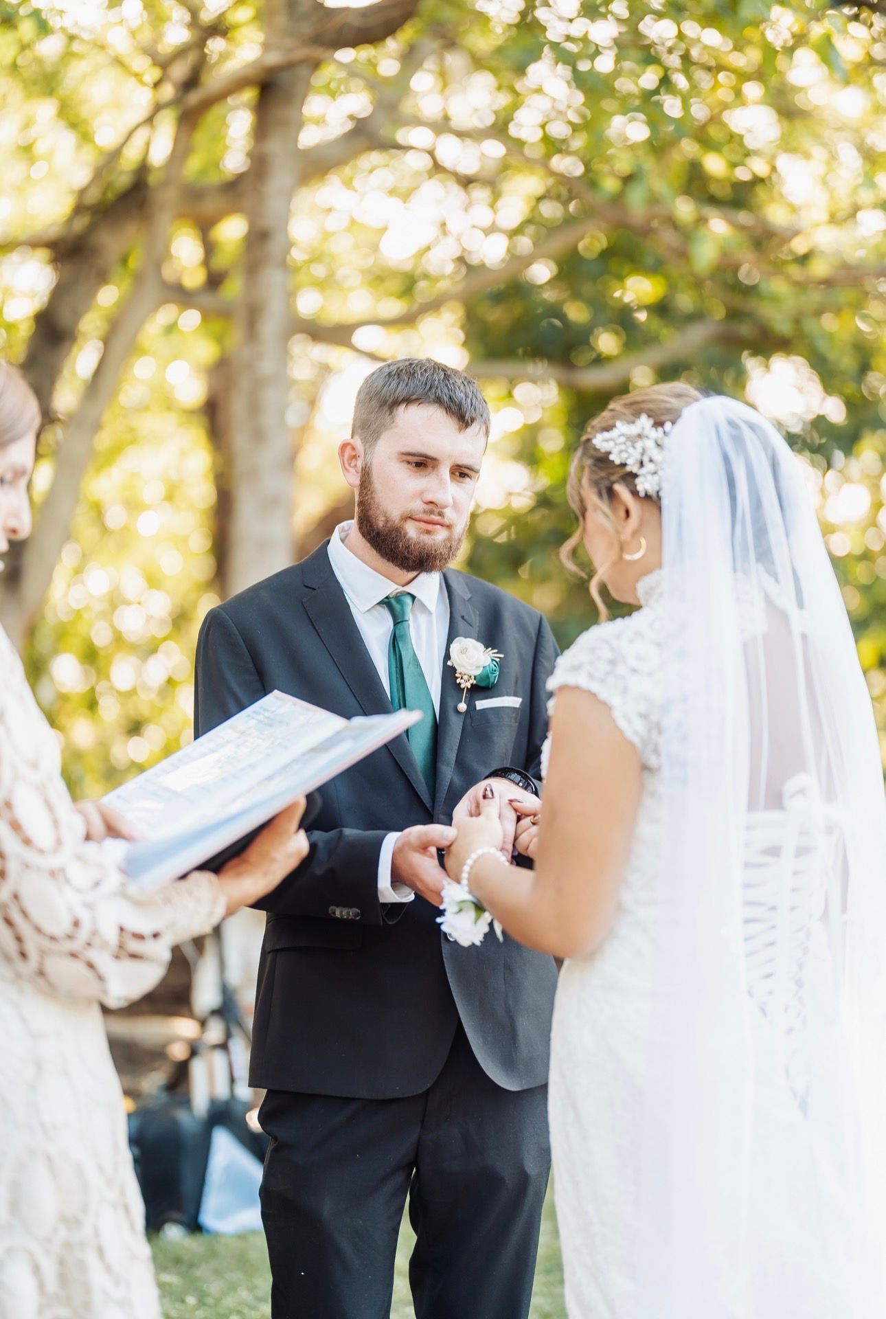 Bride and groom exchanging vows outdoors under sunlit trees