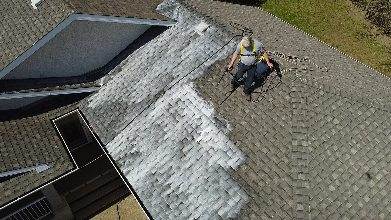 An aerial view of a man cleaning the roof of a house.
