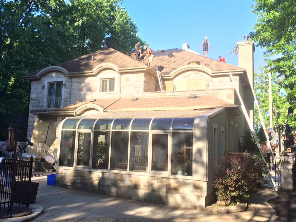 Des couvreurs remplacent les tuiles d'une maison avec véranda. La lumière du soleil illumine la structure.