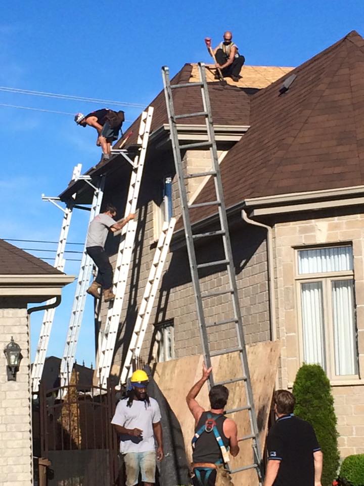 Des ouvriers du bâtiment travaillent sur un toit, utilisant plusieurs échelles pour y accéder.