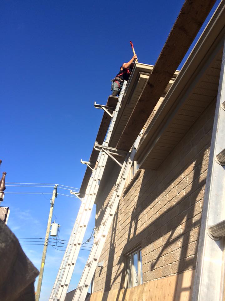 Une personne sur une échelle travaille sur le toit d'un bâtiment sous un ciel bleu dégagé.