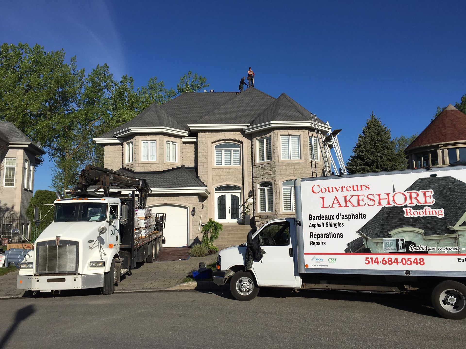 Camions et ouvriers sur un toit, se préparant à poser de nouveaux bardeaux sur une maison à deux étages.