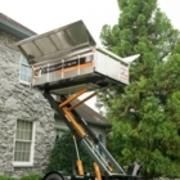 Un camion élévateur soulève un conteneur à côté d'un bâtiment en pierre ; feuillage vert en arrière-plan.
