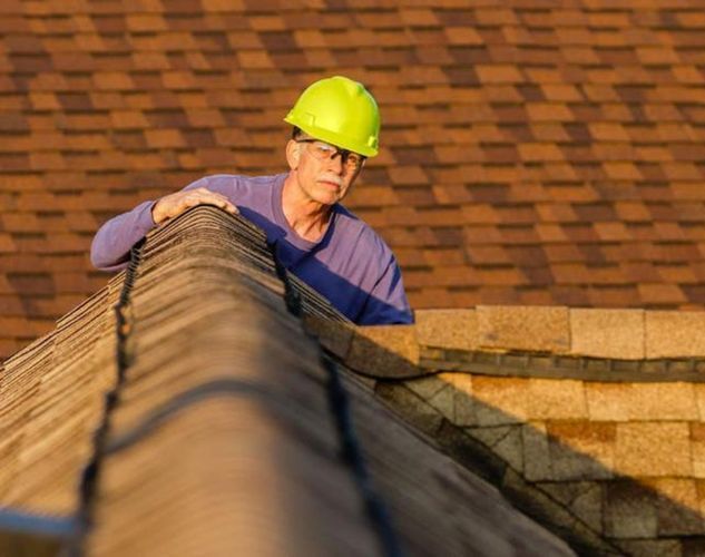 A man wearing a yellow hard hat is working on a roof.