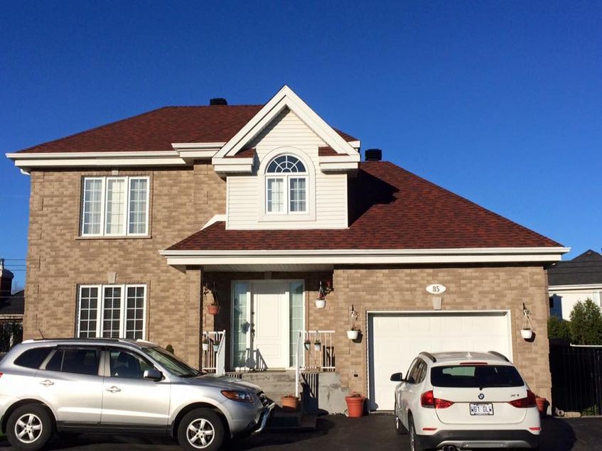 Two cars are parked in front of a house with a red roof