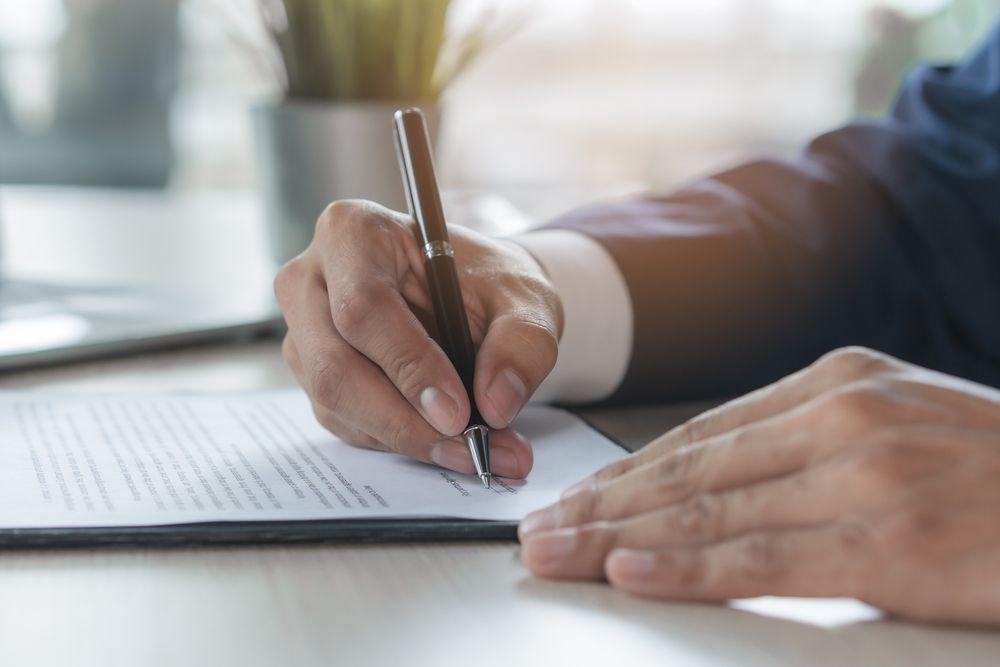 Les mains d'une personne écrivant au stylo sur un document.