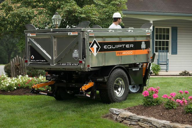 Mini-benne Equiptter grise et orange sur une pelouse résidentielle, avec une personne portant un casque de chantier debout à l'intérieur.