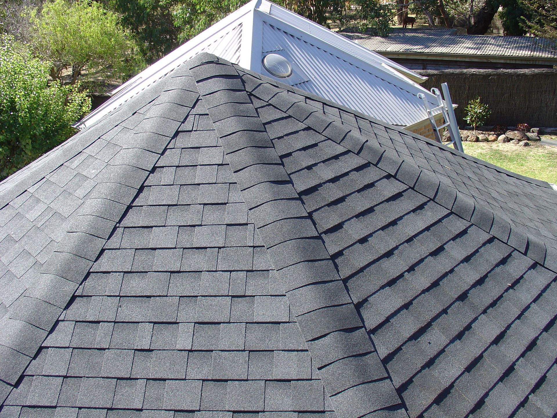 Toiture en bardeaux d'asphalte gris sur une structure à plusieurs pans, contrastant avec une toiture métallique blanche en arrière-plan.