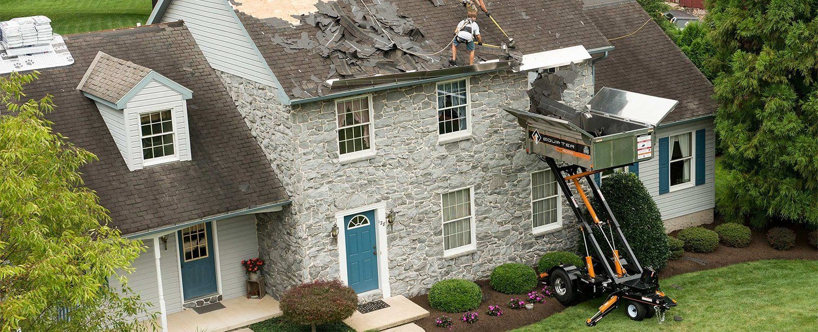 Une maison en cours de réparation de toiture, avec une machine transportant de vieux bardeaux.