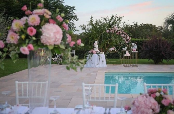 Ricevimento di nozze a bordo piscina con centrotavola floreali rosa e sedie bianche al crepuscolo