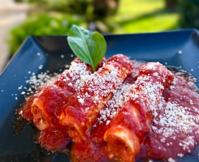 Piatto di pasta al sugo rosso guarnita con formaggio grattugiato e una foglia di basilico su un piatto scuro