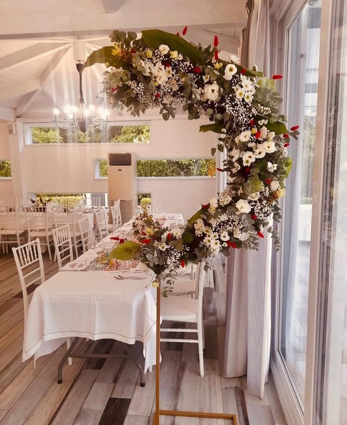 Un arco a forma di cuore ricoperto di fiori accanto a un tavolo decorato in un luminoso tendone per eventi.