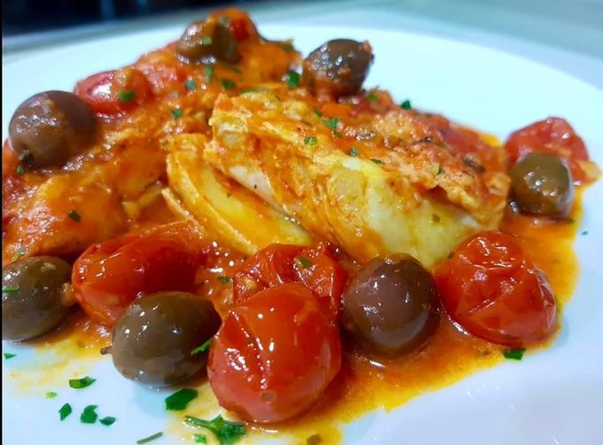 Pesce al forno in salsa di pomodoro con pomodorini e olive su un piatto bianco