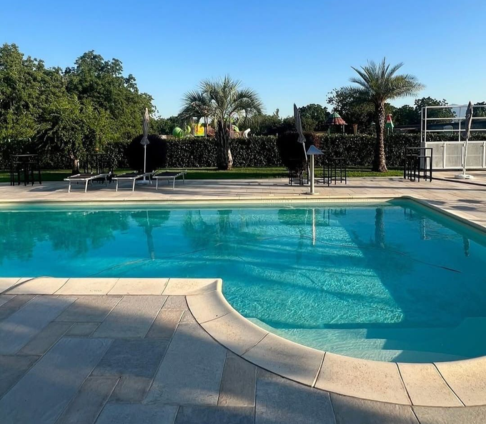 Piscina all'aperto con acqua cristallina, pavimentazione in pietra e palme lungo la recinzione.