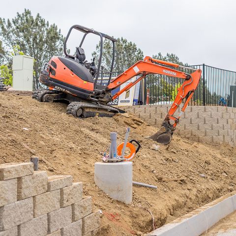 Orange excavator on a dirt hill near a retaining wall, preparing a construction site.