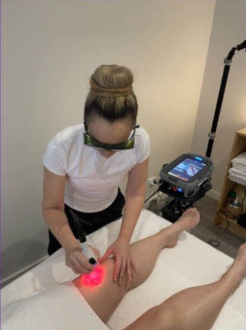 Person receives leg massage from a handheld device on a treatment table in a clinic room