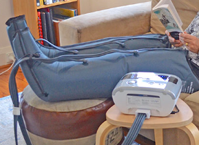 Blue leg compression boots connected to a white pump beside a person sitting on a chair