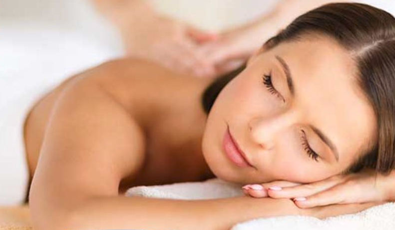 Woman resting face down on a massage table with eyes closed, receiving a shoulder massage