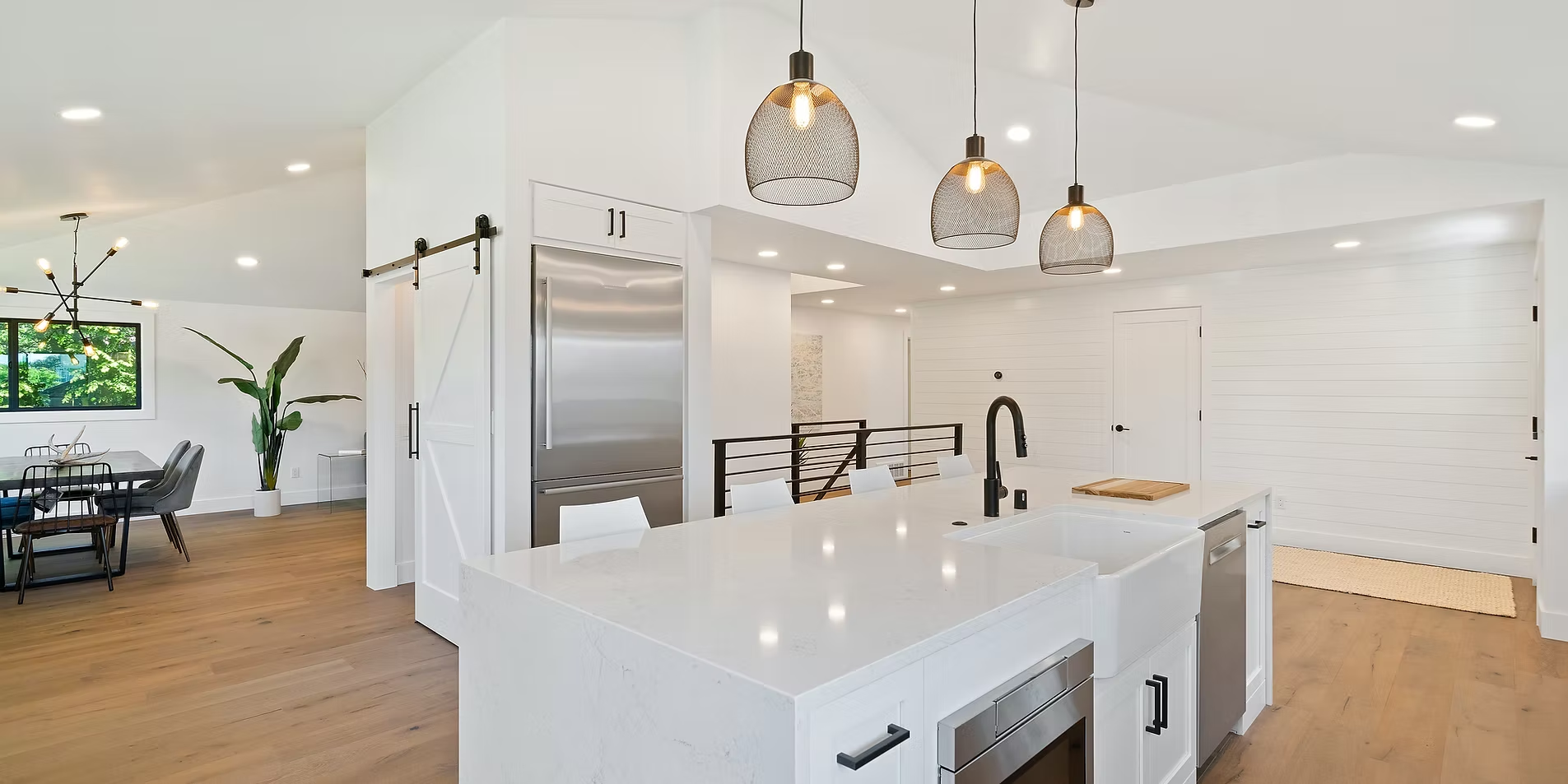 Bright modern kitchen with white island, pendant lights, and open dining area in the background