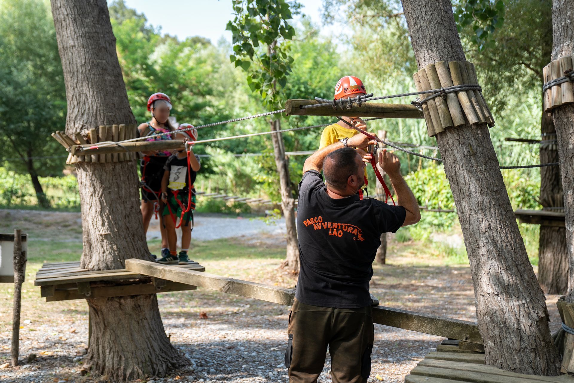 Due persone con il casco affrontano un percorso a ostacoli tra le corde di un parco boschivo.