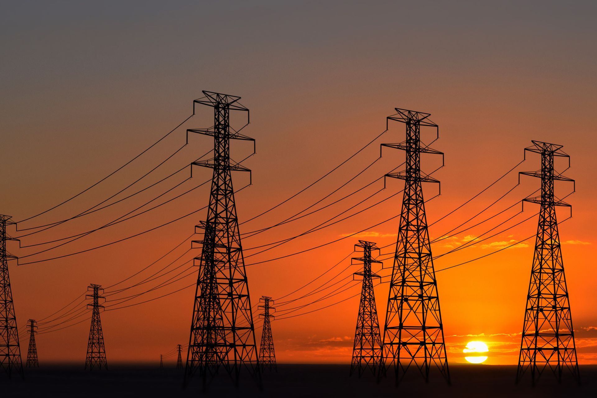 A row of power lines are silhouetted against a sunset sky