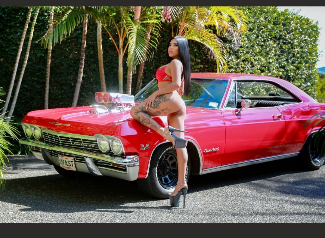 Woman posing beside a red classic car on a palm-lined street