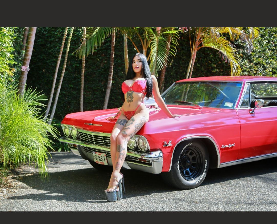 Woman posing beside a red classic car in a tropical driveway